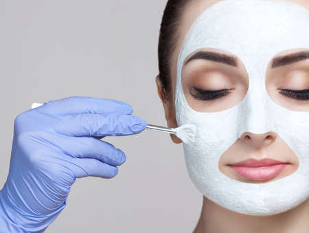 The cosmetologist applying mask with stick to the face of a young woman in beauty salon.の写真素材