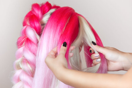The hairdresser weaves braids with pink kanekalons beautiful blonde beauty salon.の写真素材