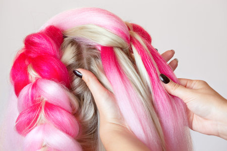 The hairdresser weaves braids with pink kanekalons beautiful blonde beauty salon.の写真素材