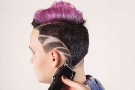 Hairdresser cuts hair with clipper.  Portrait of a beautiful young teenager with a beautiful creative hairstyle, hair painted in pinkの写真素材