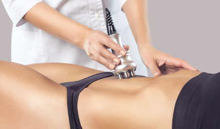 The doctor does the Rf lifting procedure on the stomach and hips of a woman in a beauty parlor. Treatment of overweight and flabby skin.の写真素材
