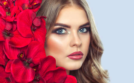 Portrait of a woman with beautiful make-up holds a red orchid in his hands. Professional makeup and skin care.の写真素材