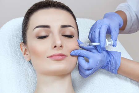 The doctor cosmetologist makes the Rejuvenating facial injections procedure for tightening and smoothing wrinkles on the face skin of a beautiful, young woman in a beauty salon.Cosmetology skin care.の写真素材