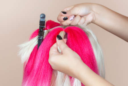 The hairdresser weaves braids with pink kanekalons beautiful blonde beauty salon.Beautiful hairstyles.の写真素材