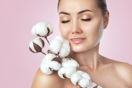 Portrait of a beautiful woman with beautiful make-up, with cotton flower in her hand on a pink background. Cosmetology and professional skin care.の写真素材