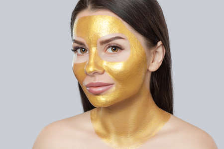 Portrait of a brunette woman who makes a golden mask on her face, neck and collarbones against aging, sagging skin and skin care.Cosmetology concept.の写真素材