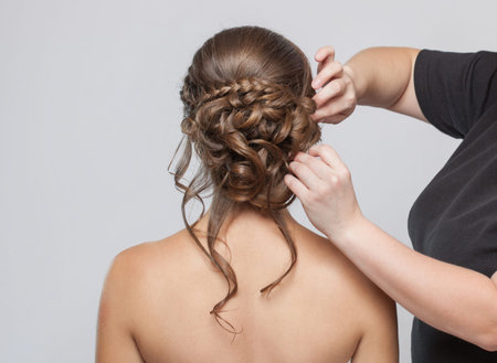 Portrait of a beautiful sensual light brown haired woman with a wedding hairstyle in a beauty salon. The hairdresser does the hairstyle. Wedding hairstyle.の写真素材
