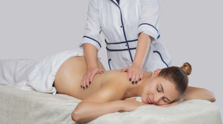 Masseur makes a relaxing massage on the neck, shoulders and  back of a young beautiful woman in a spa. Cosmetology and massage concept.の写真素材