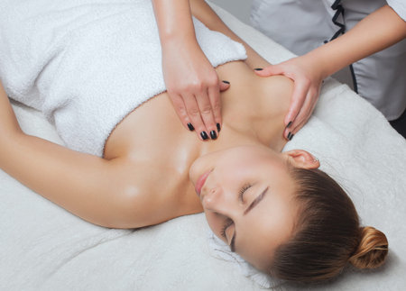 Masseur makes a relaxing massage on the face, neck, shoulders and collarbones of a young beautiful woman in a spa. Cosmetology and massage concept.の写真素材
