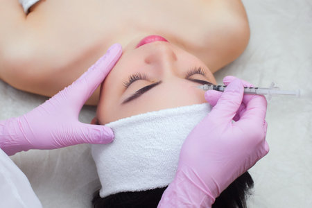 Cosmetologist does anti-aging procedures on the face of a beautiful woman with clean skin in a...