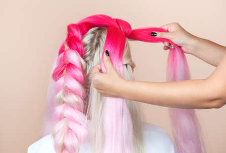 The hairdresser weaves braids with pink kanekalons beautiful blonde beauty salon.Beautiful hairstyles.の写真素材