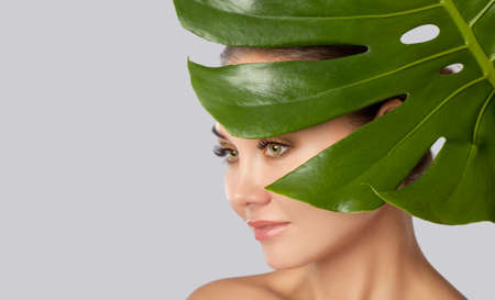Portrait of a beautiful happy woman with long eyelashes, beautiful fresh nude make-up, with clean skin on the background of a leaf of monstera.  Professional makeup and cosmetology skin care.の写真素材