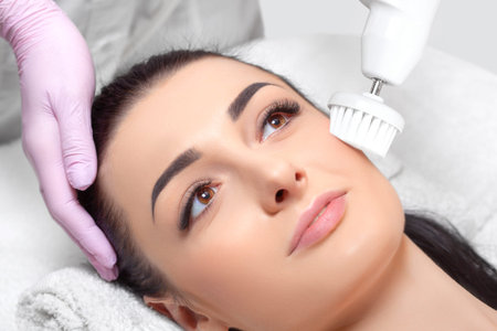 The cosmetologist makes the Hardware face cleaning  procedure with a soft rotating brush of a...