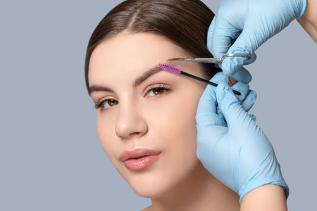 Makeup artist comb and trim the eyebrows with scissorss to a woman before staining with henna....