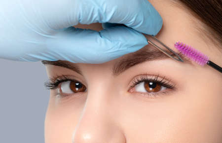 Makeup artist plucks eyebrows with tweezers to a woman before staining with henna. Women's cosmetology in the beauty salon.の写真素材