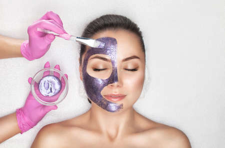 Beautician makes a face mask with purple particles on the face of a woman to rejuvenate the skin. Cosmetology treatment of problem skin on the face and body.の写真素材