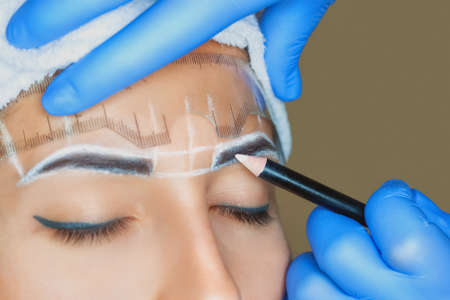 Permanent make-up for eyebrows of beautiful woman with thick brows in beauty salon. Closeup beautician doing tattooing eyebrow. Professional makeup and cosmetology skin care.の写真素材