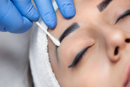 Permanent make-up for eyebrows of beautiful woman with thick brows in beauty salon. Closeup...