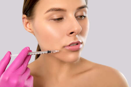 Woman with beautiful clean skin. Cosmetologist does injections for lips augmentation and anti wrinkle in the nasolabial folds of a beautiful woman. Women's cosmetology in the beauty salon.の写真素材