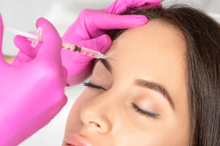 Woman at the beautician. Cosmetologist does anti wrinkle injections on the forehead and between eyebrows. Women's cosmetology in the beauty salon.の写真素材