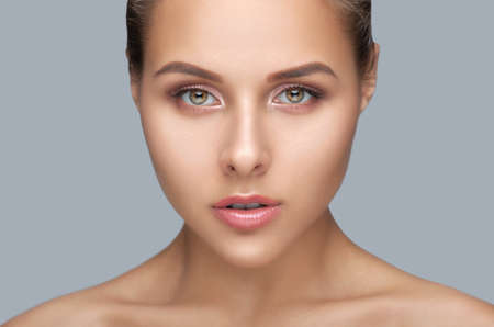 Portrait of a beautiful woman with brown hair, beautiful fresh make-up and with healthy clean skin on a gray background. Make-up and cosmetology concept.の写真素材