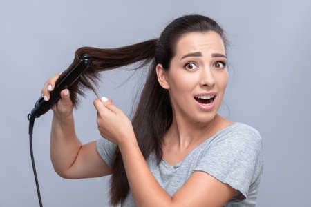Young woman makes curly hair straightening.Portrait of a beautiful girl with long dark hair, clean skin.She curls during the procedure.The concept of hair care at home, creating hairstyle, hair treatmentの写真素材