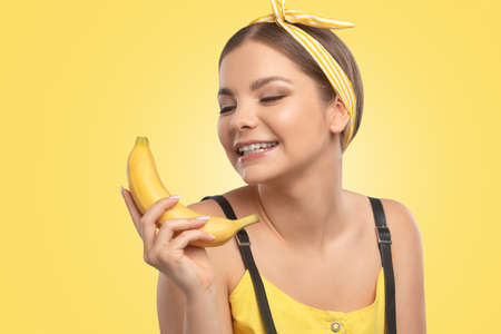Portrait of a beautiful brunette girl with healthy clean skin and fresh make-up on a yellow background. She holds a banana. Healthy nutrition concept.の写真素材