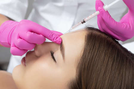 Woman at the beautician. Cosmetologist does anti wrinkle injections on the forehead and between eyebrows. Women's cosmetology in the beauty salon.の写真素材