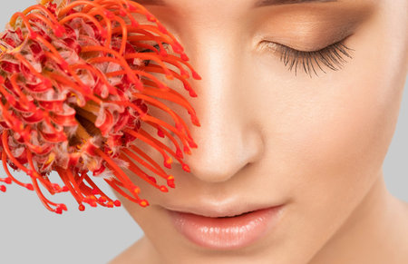 Portrait of a charming girl with flower, with makeup, lush eyebrows and plump lips. Personal care, cosmetology and makeup concept.の写真素材