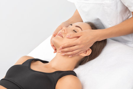 Masseur makes a relaxing massage on the face, neck, shoulders and collarbones of a young beautiful woman in a spa. Cosmetology and massage concept.の写真素材