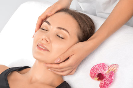 Masseur makes a relaxing massage on the face, neck, shoulders and collarbones of a young beautiful woman in a spa. Cosmetology and massage concept.の写真素材