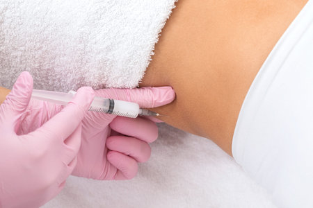A doctor of aesthetic cosmetology makes lipolytic injections to burn body fat on a woman's stomach...