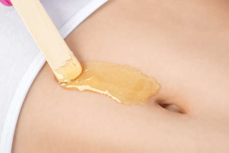 A beautician makes a sugar paste depilation of a woman's belly in a beauty salon. Female aesthetic cosmetology.の写真素材