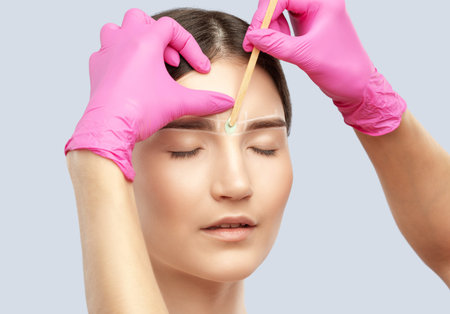 Makeup artist does facial hair removal procedure. Beautiful girl with blue eyes having Permanent...