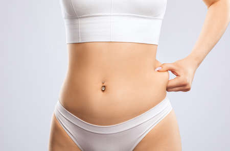 Girl pulls the skin on the abdomen, showing the body fat in the abdominal area and sides. Treatment and disposal of excess weight, the deposition of subcutaneous fat.の写真素材