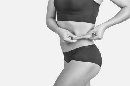 Girl pulls the skin on the abdomen, showing the body fat in the abdominal area and sides. Treatment and disposal of excess weight, the deposition of subcutaneous fat.の写真素材