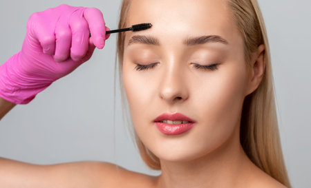 Makeup artist combs and plucks eyebrows after dyeing in a beauty salon.Professional makeup and...