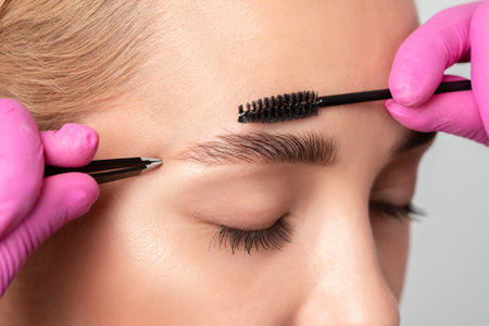 Makeup artist combs and plucks eyebrows after dyeing in a beauty salon.Professional makeup and...