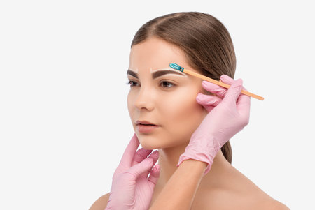 Makeup artist does facial hair removal procedure. Beautiful girl with blue eyes having Permanent...