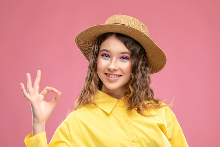 Cheerful girl with curly hair with a beautiful bright make-up in a yellow dress and a straw hat.の写真素材