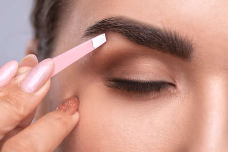 Makeup artist combs and plucks eyebrows in a beauty salon. Professional make-up and cosmetic skin care.の写真素材