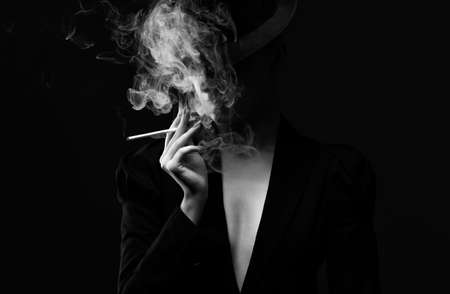 A mysterious woman in a black suit and hat smokes a cigarette. black and white photo.の写真素材