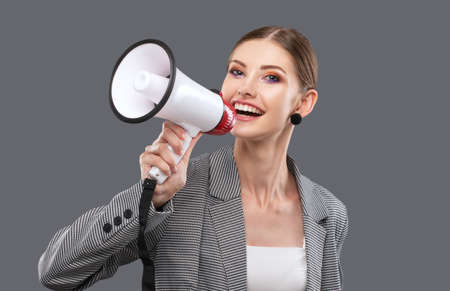 A beautiful joyful girl shouts into the loudspeaker on an isolated pink background.の写真素材