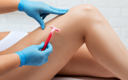 The beautician shaves the hairs on the leg of a woman in a beauty salon. Removal of unwanted body...