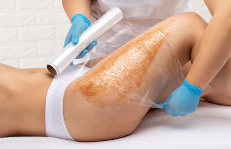 The beautician makes a cosmetic peeling procedure on the thighs of a woman. Spa procedures in a beauty salon.の写真素材