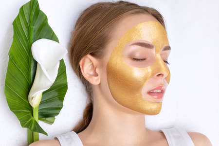 Beautician makes a gold face mask of a woman to rejuvenate the skin. Cosmetology treatment of problem skin on the face and body.の写真素材