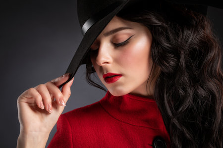 A slender brunette woman with long curly hair and beautiful makeup, she is wearing a red coat.の写真素材