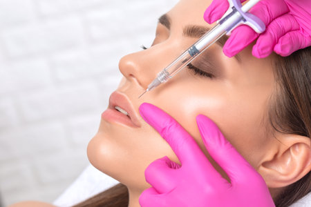 Cosmetologist does injections for lips augmentation and anti wrinkle in the nasolabial folds of a beautiful woman. Women's cosmetology in the beauty salon.の写真素材