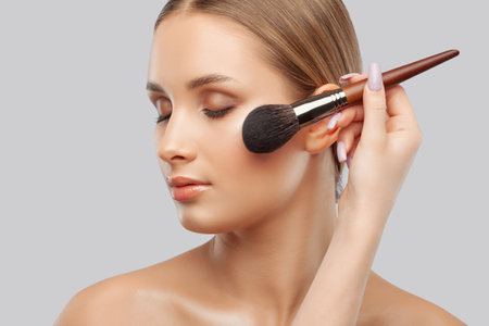 Portrait of a beautiful brunette girl with beautiful fresh makeup and healthy clean skin.Makeup artist holds a powder brush in her hands. professional makeup conceptの写真素材