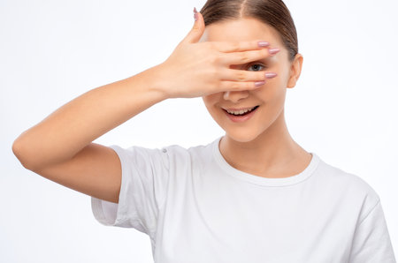 Beautiful young pensive woman with clean skin in a white T-shirt covered her face with her hand. Makeup and healthy clear skin.の写真素材